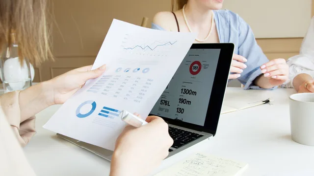 Close-up of professionals reviewing financial charts and data on laptop in a meeting. Markteintritte und Marktaustritte erkennen: Register und Statistik nutzen
