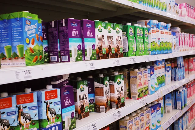 Various colorful boxes of milk placed on shelves with prices in modern supermarket. Preise beobachten in Österreich: Quellen, Methoden und Dokumentation